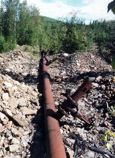 long rusty pipe running along a rocky surface in a forest