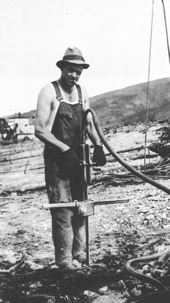 man in overalls standing next to a device stuck in the ground