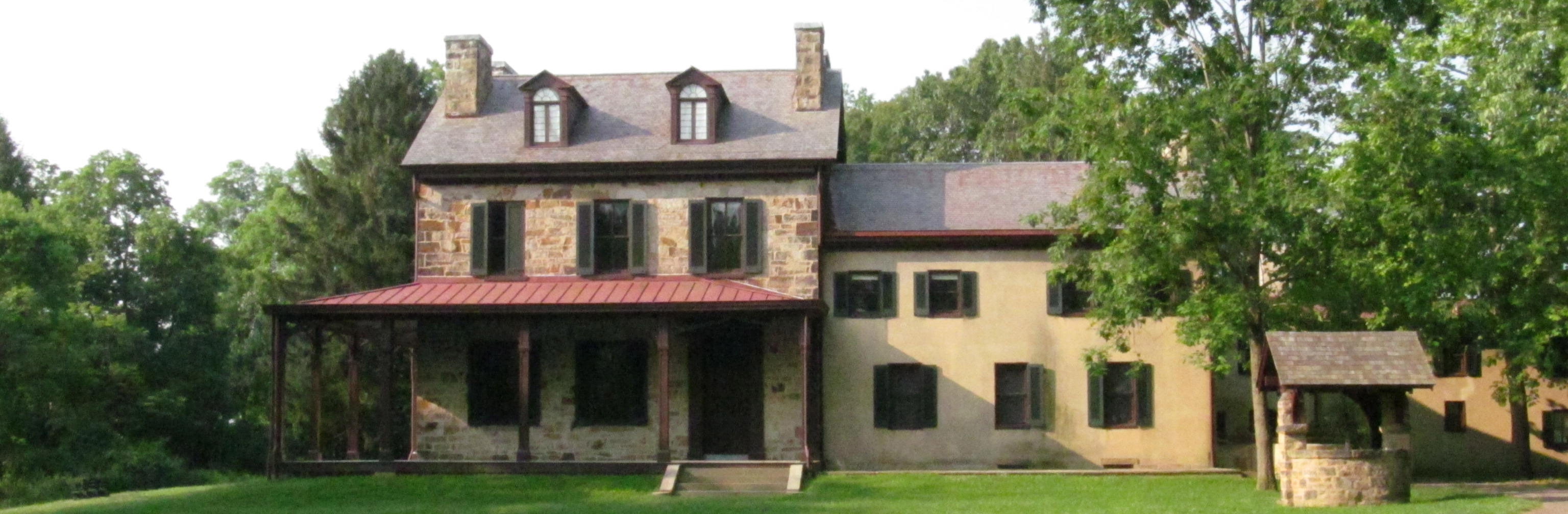 View of the front of the stone portion of the Gallatin House with green trees in the background.