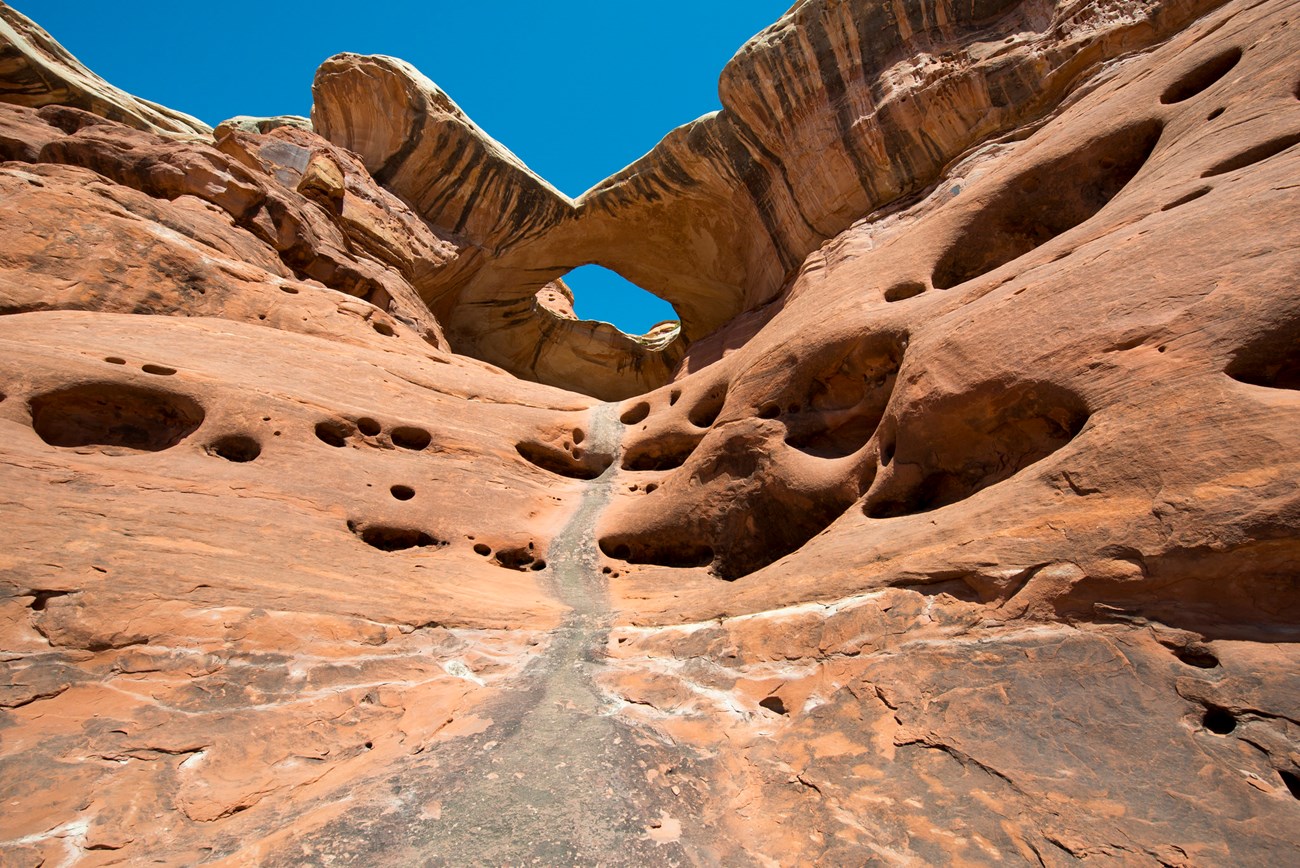 Photo of red rock slope with holes and an arch