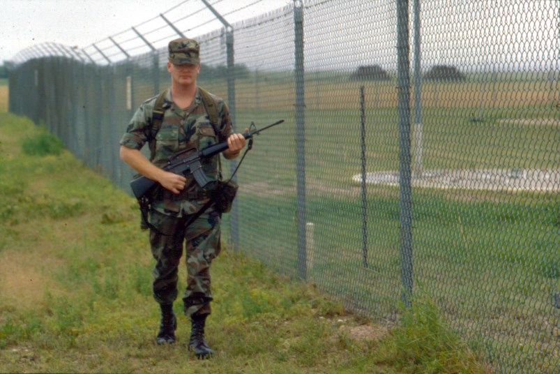 A uniformed airman with a weapon patrols a fence-line