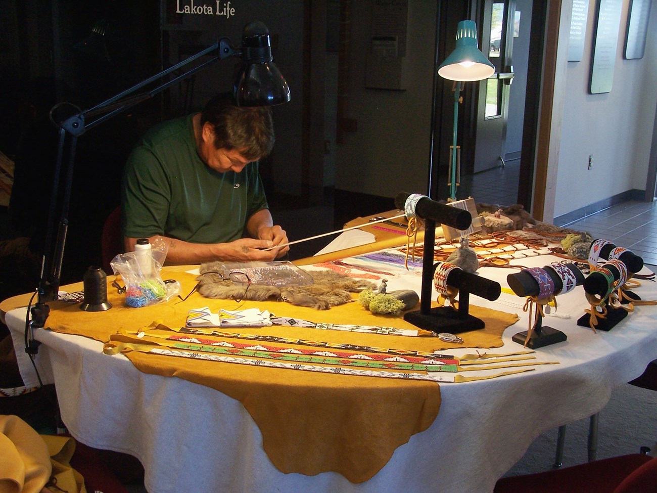 Man working on a loom at a table covered in textiles