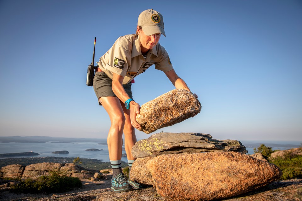 Woman lowers a rock onto a pile used as a trail marker
