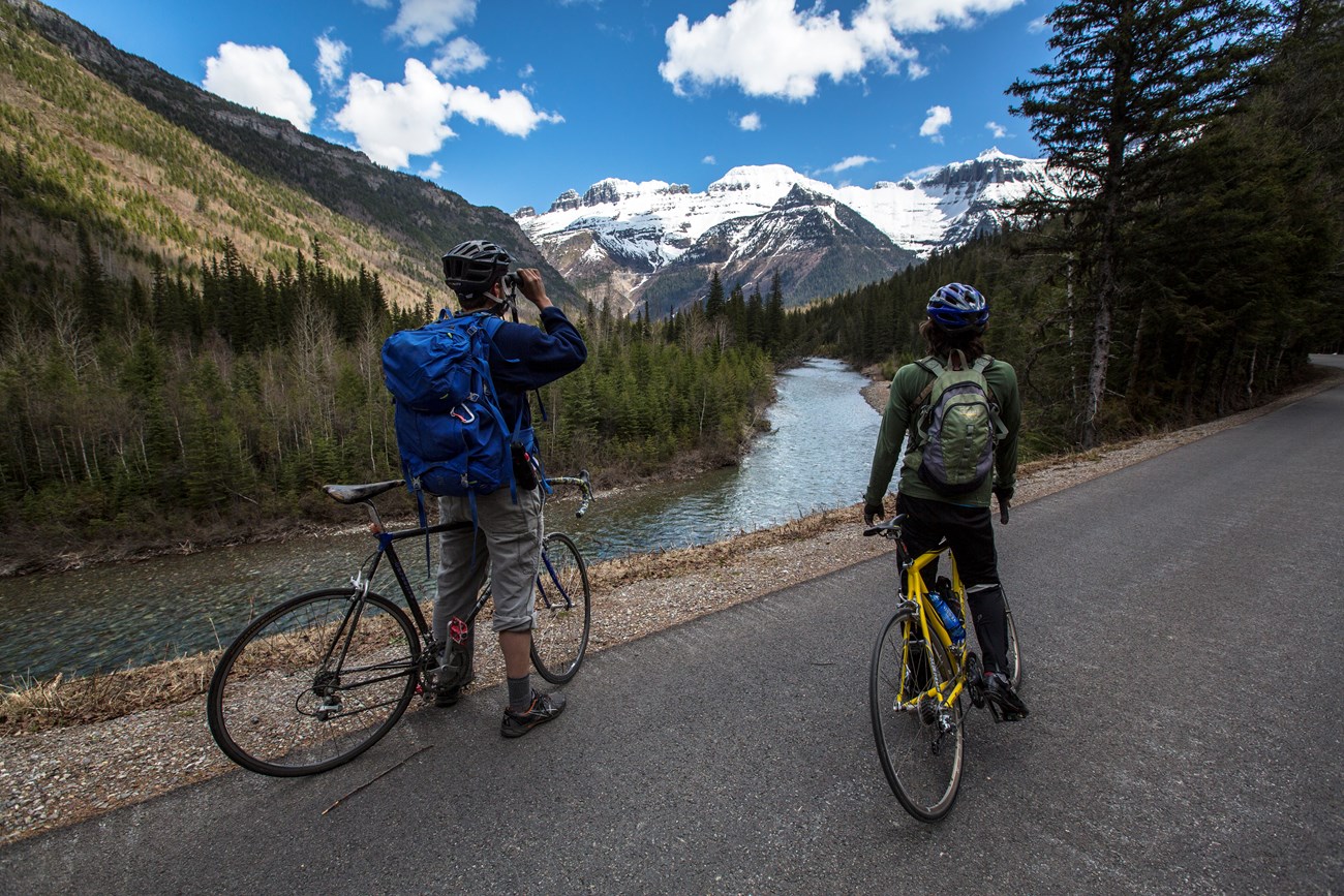 two bicyclists looking at ice top mountain from adistance with binoculars