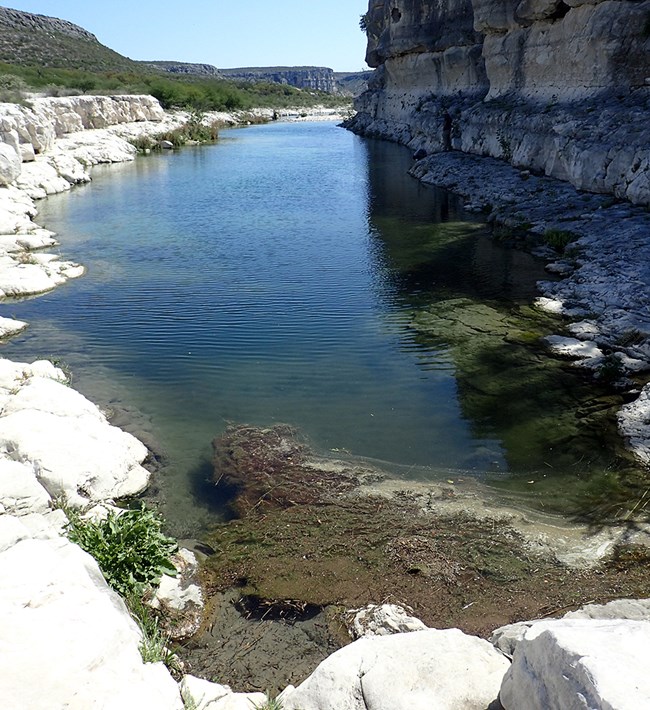 A large narrow pool of water surround by rock faces.