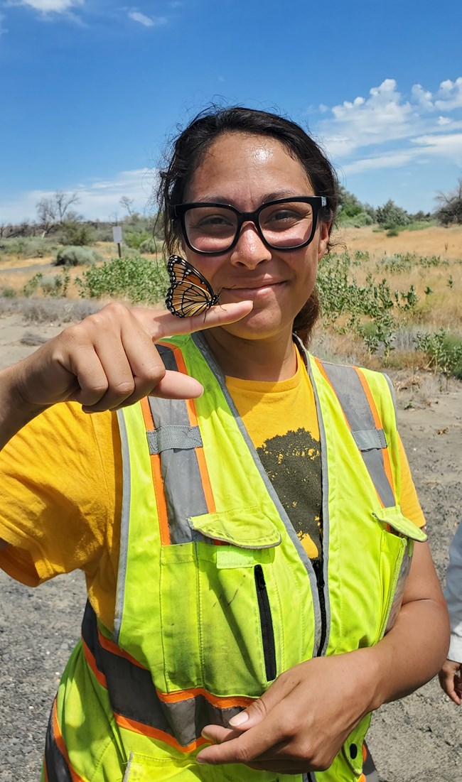 A person with an orange and black butterfly resting on her finger.