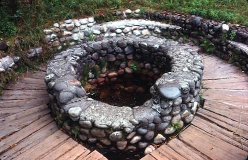 A rock wall and a boardwalk encircle a small spring.