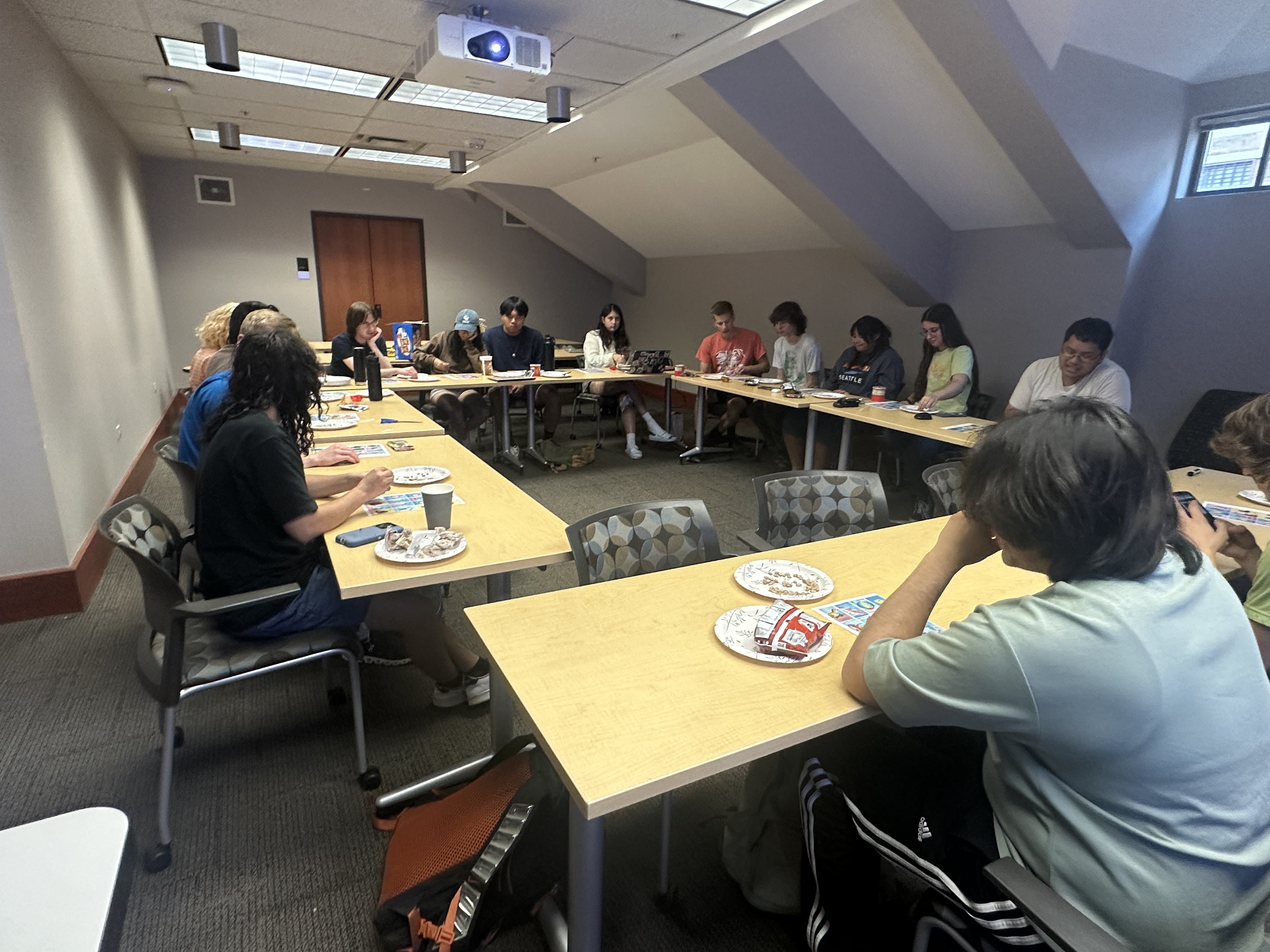 Members of the Texas Dinosaur Club are shown playing a game of Paleoteria around a set of tables in a classroom.