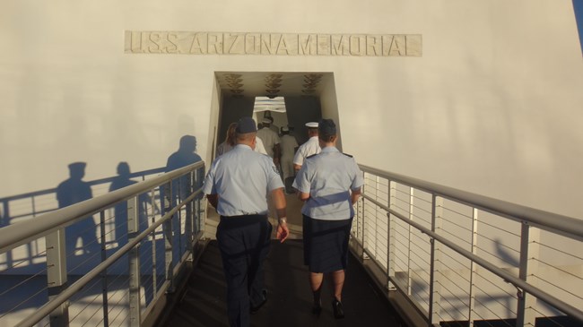People in military uniforms walk up a ramp to enter the USS Arizona Memorial.