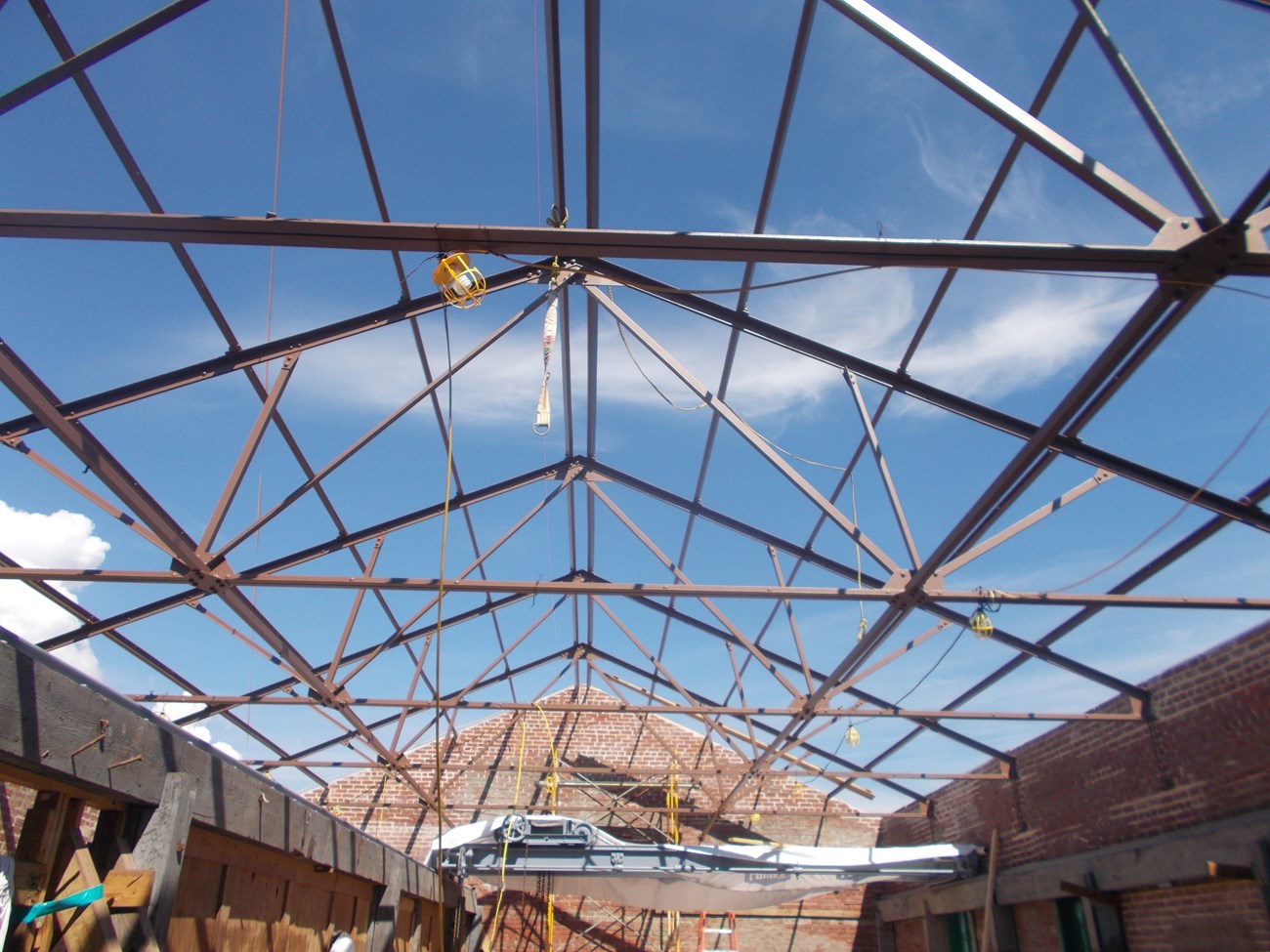 From inside a building looking up through the roof trusses to the sky.