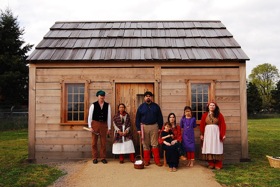 Group of men and women standing in front of a Village house.