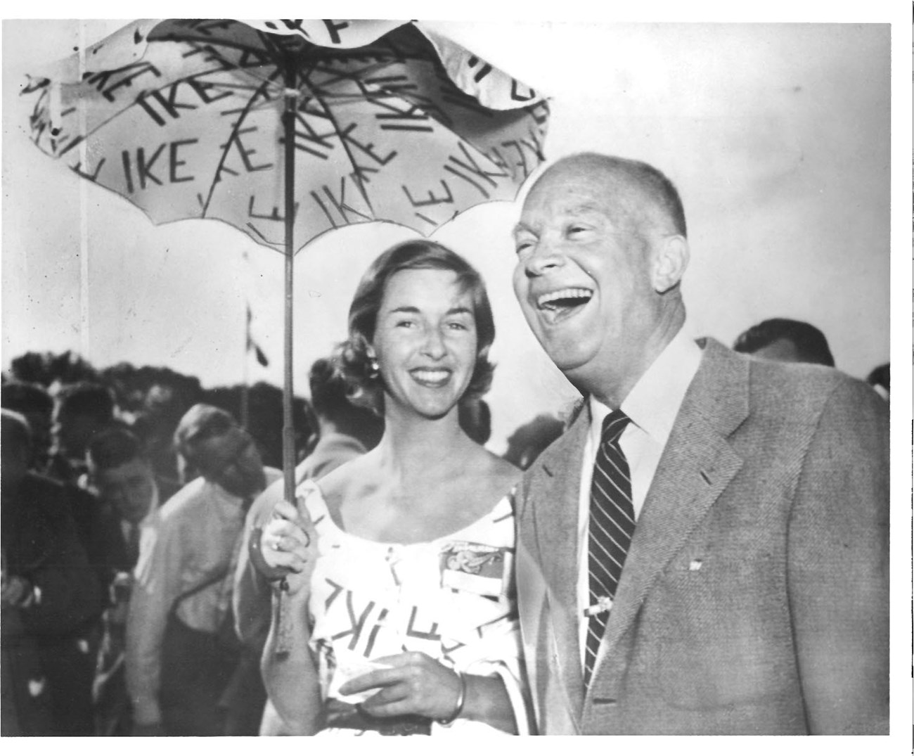 smiling woman holding umbrella stands next to laughing President Eisenhower