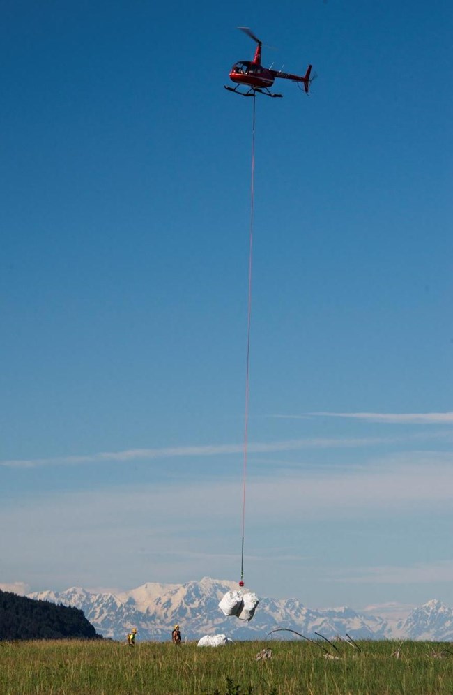 A helicopter loads large bags of marine debris using a sling