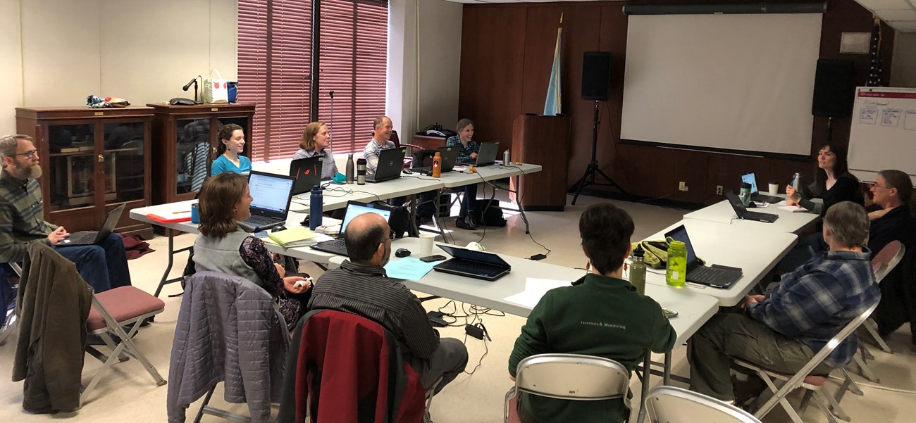 Gropu of people sitting around tables with a projector screen at the front of the room