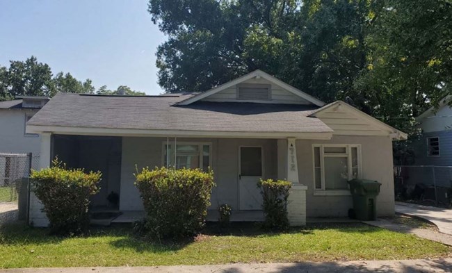 small single-story residential home with a low roof line and bushes in the front lawn
