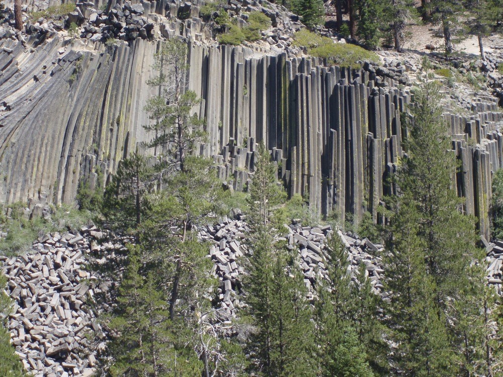 Multi-sided column rock formation with trees towering in front.