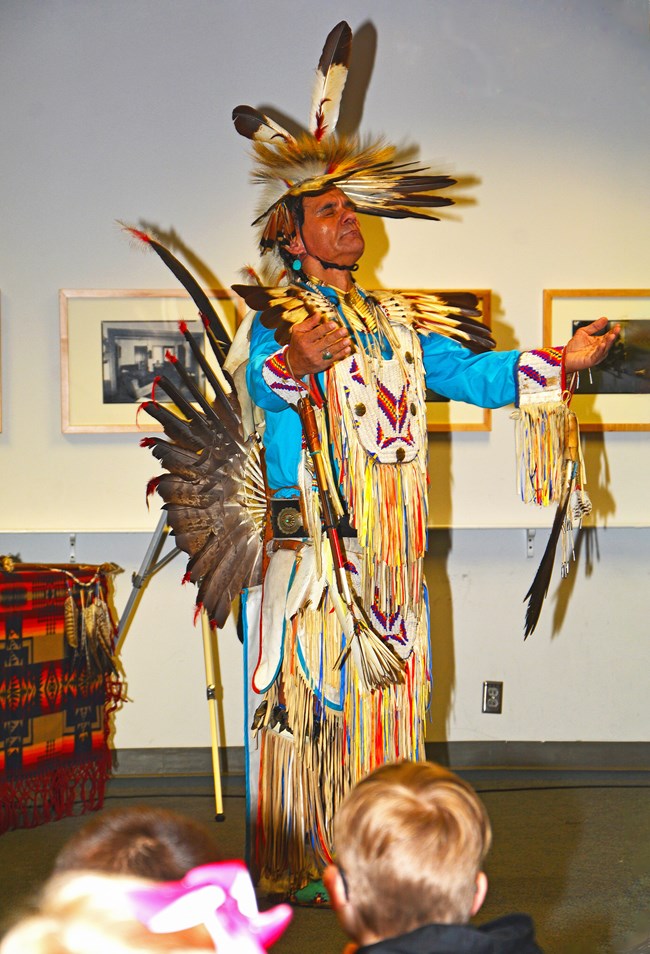 Dennis Rogers, in a traditional Navajo outfit, looks up with his eyes closed and arms outstretched during a traditional dance.