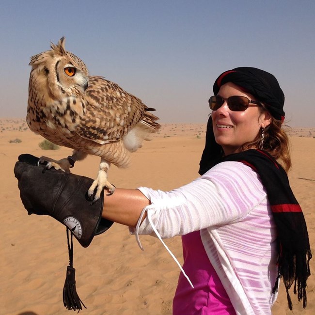 woman wearing scarf on head holding owl on outstretched gloved arm