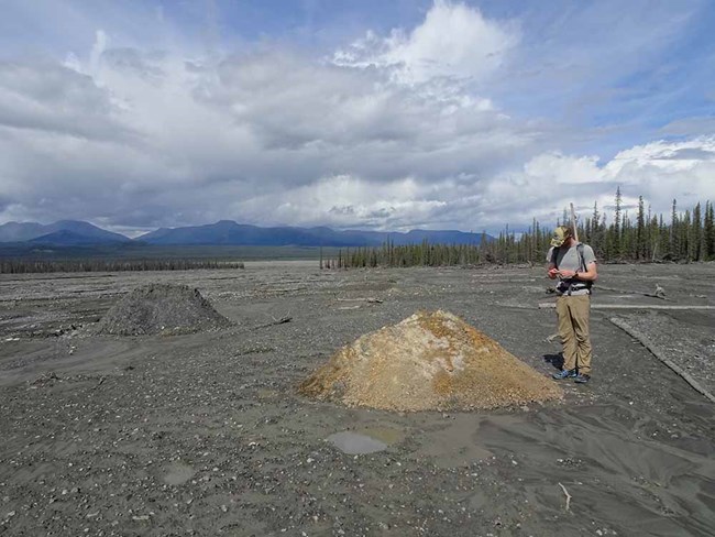 A researcher stands near a mound of rock transported by the debris flow.