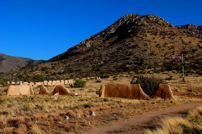Image of the fort that highlights the lime plastered ruins of Fort Bowie NHS with the American flag flying over the parade ground.