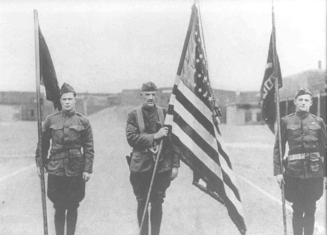 Three soldiers in World War I Uniforms holding flags