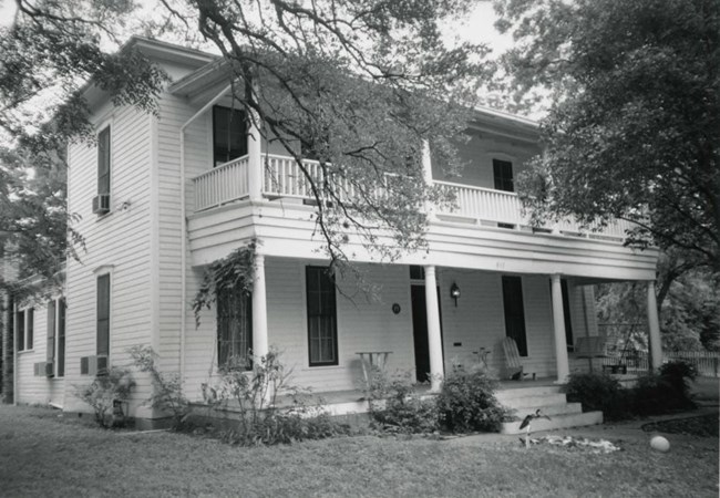 two story house with full length porches on both floors. Steps leading up to the entrance with plants around the lower level porch
