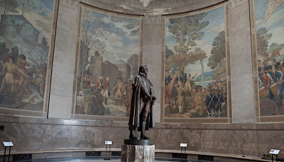 Statue of 18th century man in round memorial room surrounded by murals