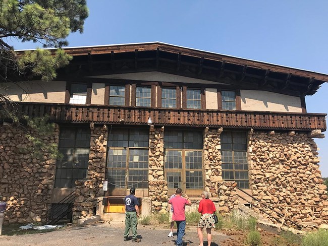 Stone and wood building with chalet-style influences. Four people are standing in front examining the building.