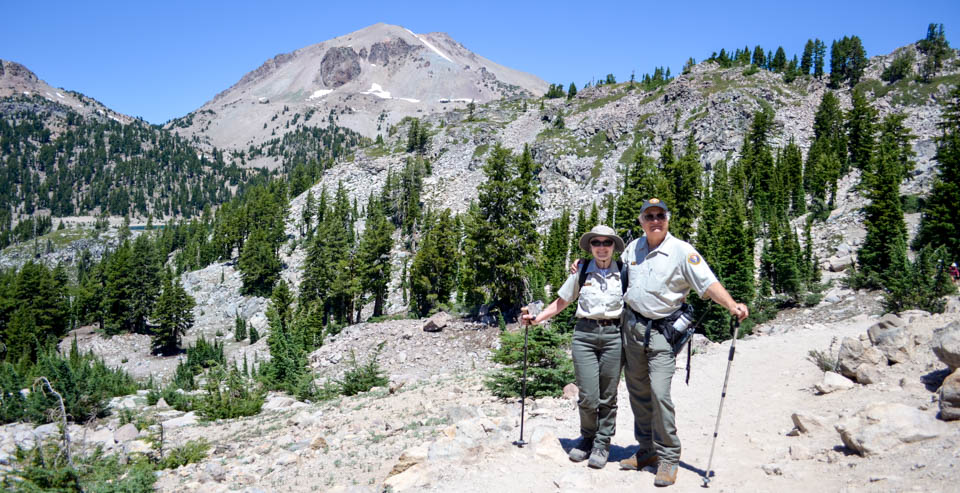 A man and a woman on a rocky trail backed by a large peak.