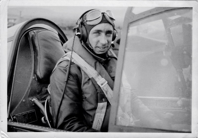 Black and white photo of a man wearing pilot goggles in an old-fashioned plane.