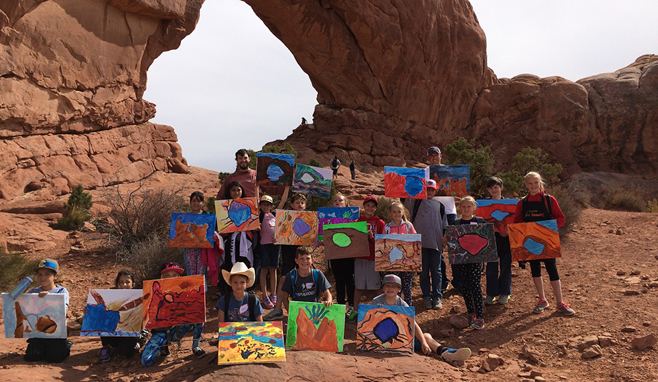 students hold pieces of art in front of a massive stone arch