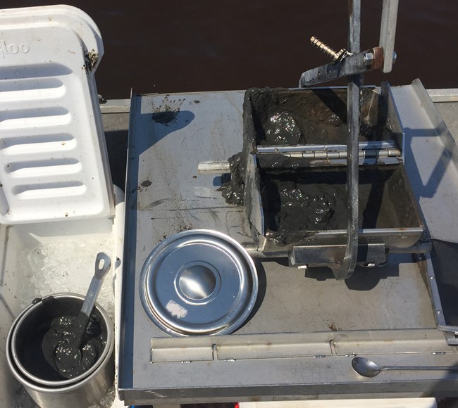 Photo of cooler on the left with sediment sample and grab sampler on a table to the right.