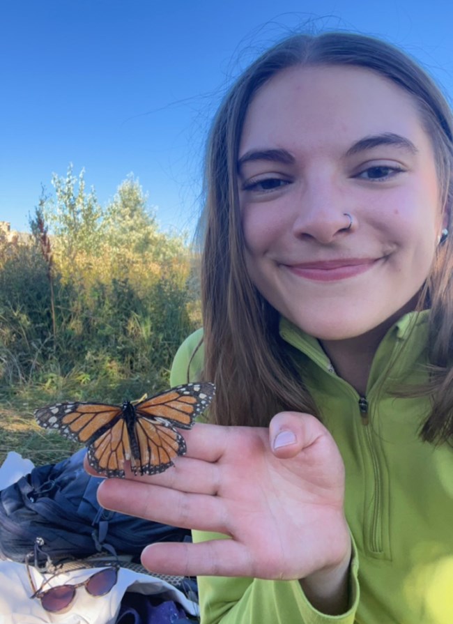 A smiling person with a monarch butterfly resting on her hand.