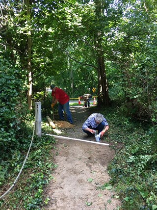 Two people work on the surface of a hard-packed dirt trail.