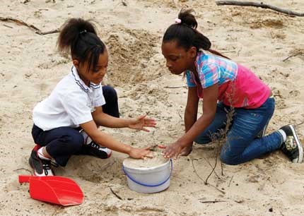 Two students dig in the sand at the Nature Play Zone