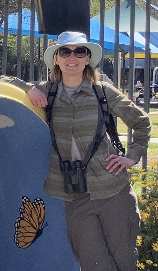 A person wearing binoculars leaning against a blue structure with a monarch butterfly painted on it.