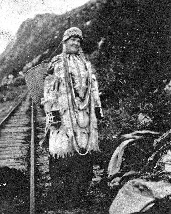 A woman standing with native decorative clothing along a railroad track