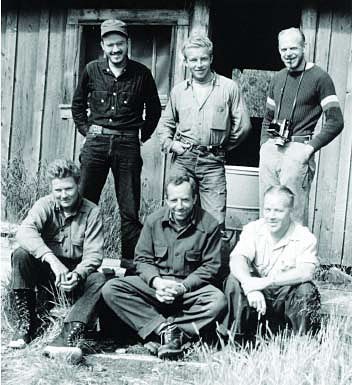 A group of six white men pose in front of an old NPS park building for the Katmai Project.