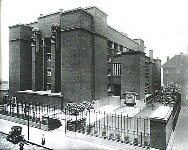 A 5 story brick building with a tall rod iron fence surrounding it.