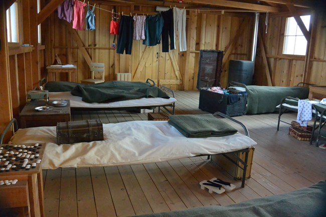 A cot with laundry hanging over it inside a recreated barracks