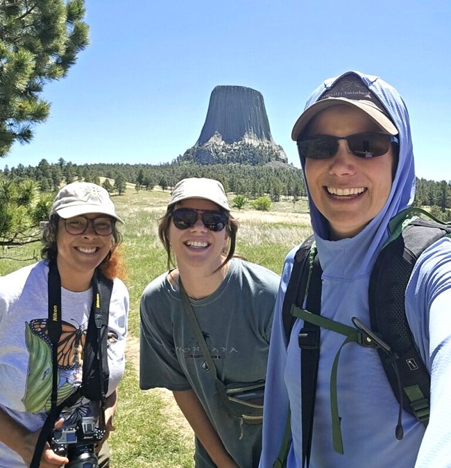 Three people smiling with Devils Tower in the background.