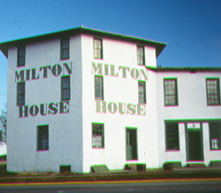 White, stone house with green painted words that say Milton House.