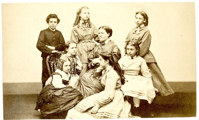 A photographic group portrait of a teacher with her 7 students