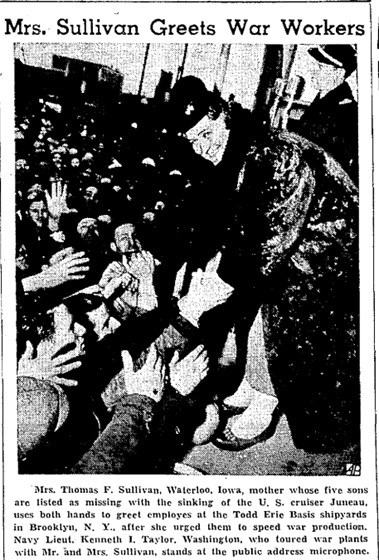 grainy newspaper image of a woman in a long fur coat reaching down and shaking hands with a large crowd of men