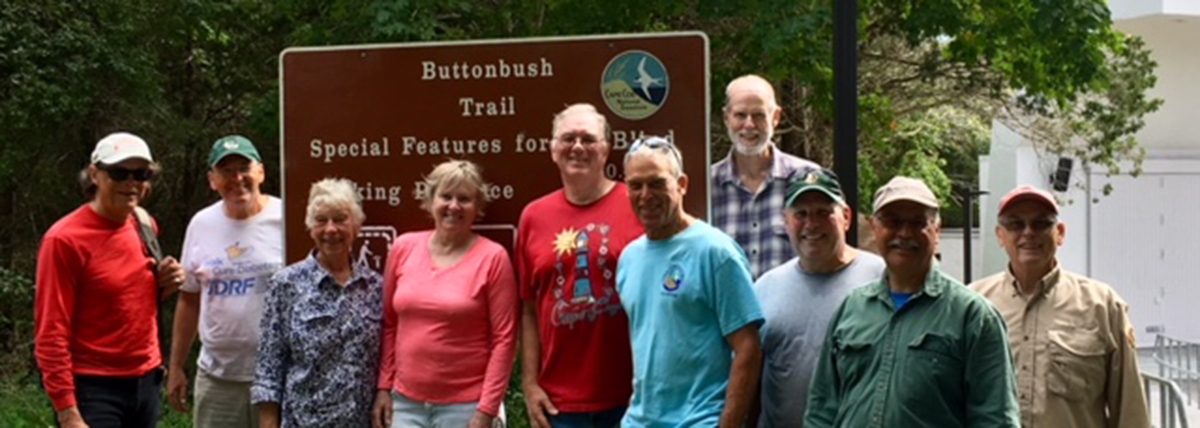A group of people stand in front of a sign that reads, "Buttonbush Trail."