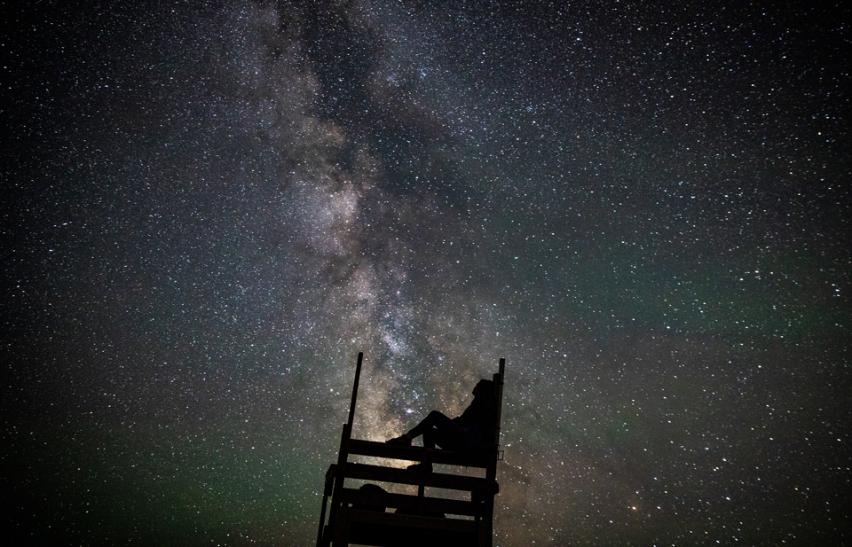 Person sitting in a lifeguard chair gazing into night sky