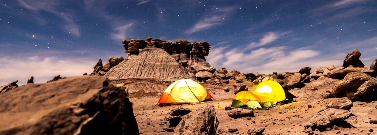 Several tents in a rocky desert under the stars at night