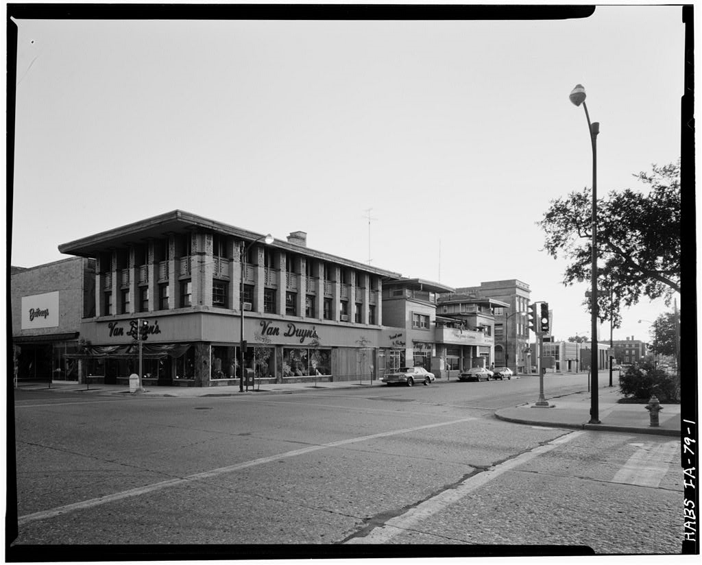 B&W photo of a building with three floors and many large windows.