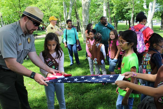 A ranger folds an American flag with a group of Girl Scouts