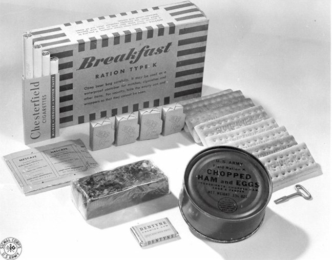 Black and white with the contents of the K-Ration breakfast arranged in front of the striped box they came in.